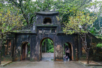 Naklejka premium A woman explores the serene grounds of the a Pagoda in The Marble Mountains, Da Nang, Vietnam. The ancient gate, adorned with moss, stands as a testament to the temple's rich history.