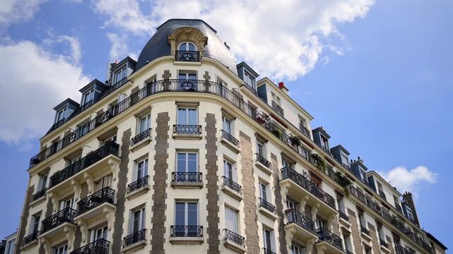 Ornate Parisian building corner with mansard roof against blue sky with clouds.
