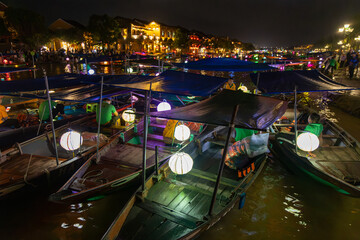 Boat operators await passengers for evening cruises on the Thu Bon River in Hoi An, Vietnam. The boats are decorated with lanterns for the popular tourist activity. © Zenstratus