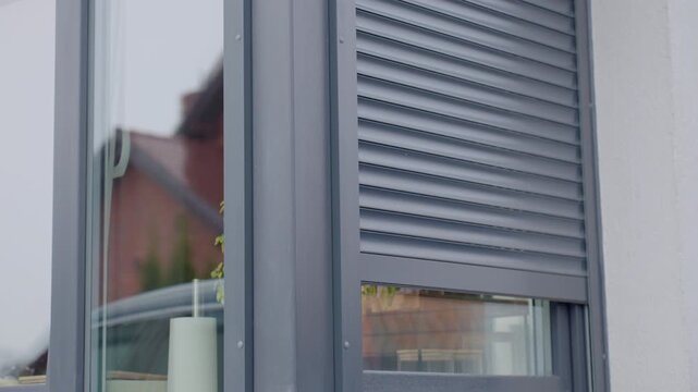 Close-up of modern exterior window with metal roller shutter moving up. Concept of home security privacy control and residential architecture detail