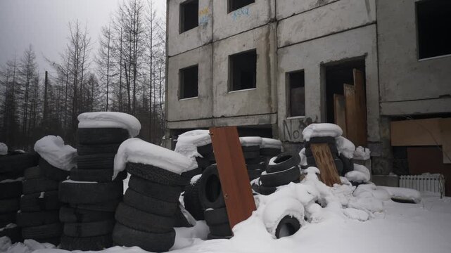 Players use tires around an abandoned building to play paintball in snowy weather.