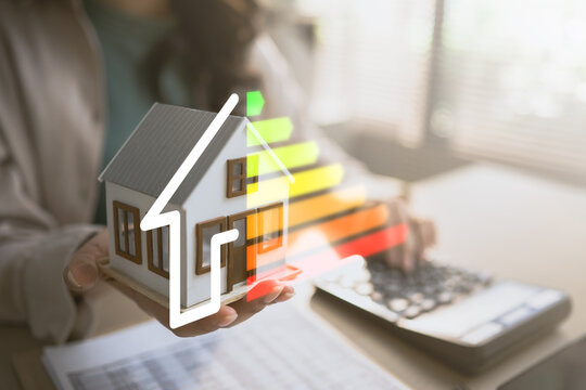 Hand holding house model with energy efficiency rating scale, representing sustainable home, energy saving, cost reduction and environmental protection.