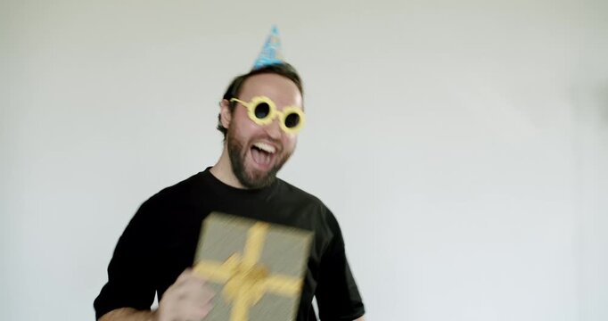 Excited man with party hat and glasses receives a surprise gift. He expresses joy and happiness. Perfect for birthdays, celebrations, holidays, or any special occasion.