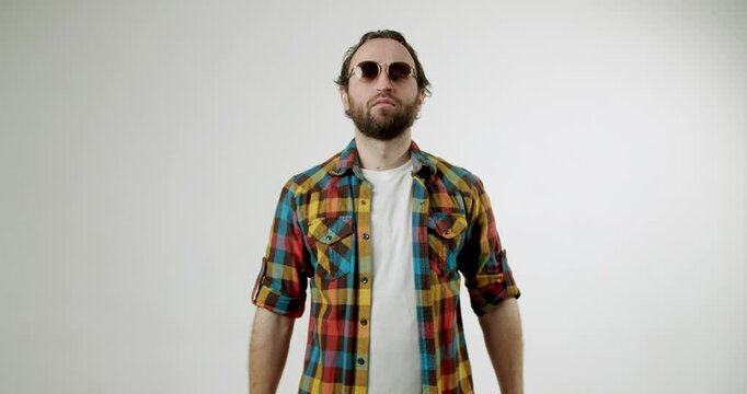 A man with a beard and sunglasses crosses his arms in an x shape to signal no or stop. He is wearing a colorful plaid shirt over a white t-shirt and is facing directly at the camera.