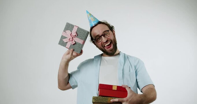 A man wearing a party hat and glasses holds a stack of gifts. He expresses excitement and surprise with his facial expressions. This video conveys feelings of celebration, joy, and appreciation.