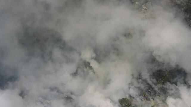 4k footage of Thick white plumes rise through dark rocky terrain, with yellow sulfur-stained inside the interior environment of Mount Bromo&rsquo;s volcano in East Java, Indonesia