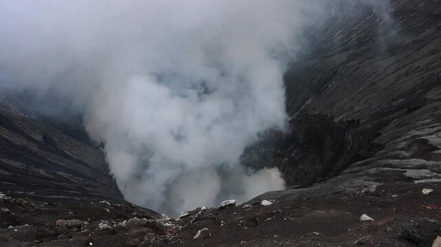 Dramatic view inside the crater of Mount Bromo volcano of thick white volcanic steam rises from active vents deep within the crater basin in in East Java, Indonesia