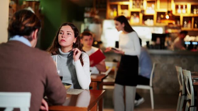 European woman happily chats with her husband while sitting in a cozy restaurant with a glass of wine. Romantic dinner for a couple in a European restaurant 