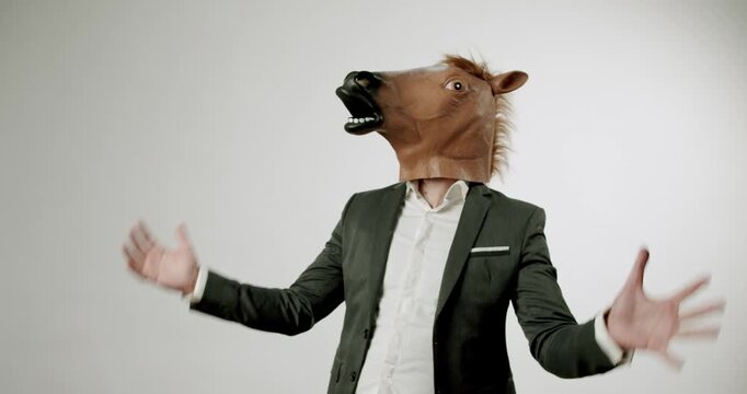 A businessman in a suit wearing a horse head mask stands against a white background. He gestures with his hands. This video evokes humor and absurdity, perfect for projects needing a comical touch.
