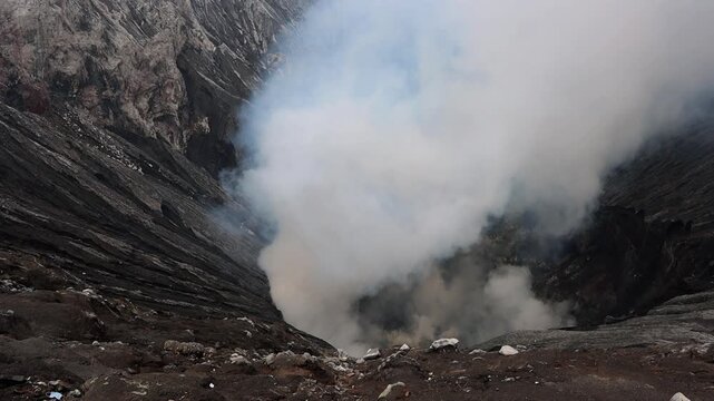 Dramatic view inside the crater of Mount Bromo volcano of thick white volcanic steam rises from active vents deep within the crater basin in in East Java, Indonesia
