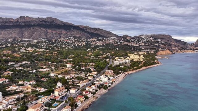 seaside town nestled below mountain, winding shoreline with terracotta roofs and pine trees, turquoise water
