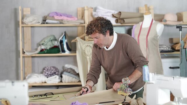 During manufacture of clothes, man tailor cuts paper dress pattern and work with hand snip, separates blanks. Process of manual production of clothes 