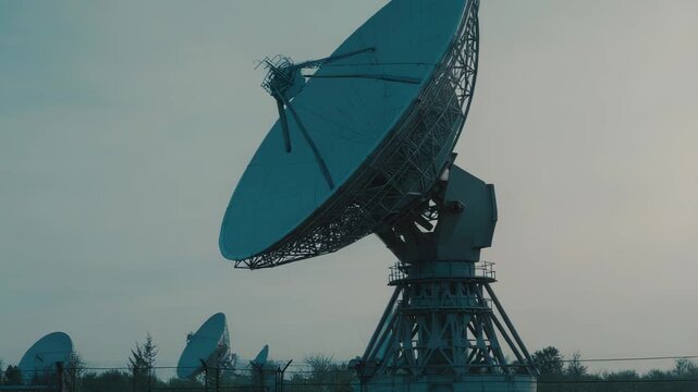 Large parabolic satellite dishes at a ground station transmit and receive signals to space, enabling global telecommunications, observation, astronomy and data transmission systems