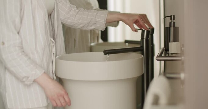 A woman is adjusting a sleek, modern faucet in a stylish bathroom setting. The bathroom features a round basin and a soap dispenser on the counter, highlighting minimalist design. Modern Faucet