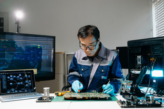 Professional senior technician holding and inspecting computer motherboard at high-tech electronics repair workstation