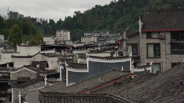 Overcast mountain town rooftops traditional buildings, dense cluster of gray tiled roofs and whitewashed walls, narrow alleys winding between courtyard houses, chimney stacks and eaves showing