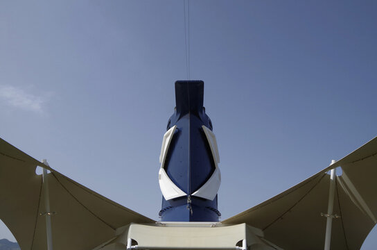 Close up detail view of modern cruiseship cruise ship liner funnel and white steel superstructure over outdoor deck against blue sky in background in blue and white