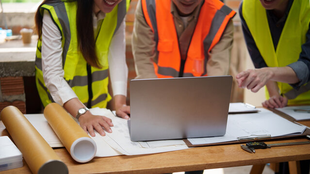 Team of construction professionals analyzing architectural drawings and digital plans on a laptop.