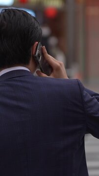 Slowmotion of Japanese businessman stands patiently in the crosswalk, using a smartphone in hand to make a business call. Asian man with mobile phone waits in zebra road.