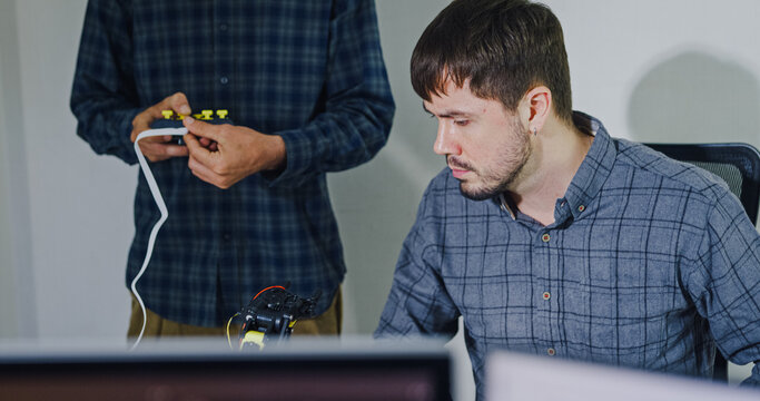 Team adult male engineer collaborate on robotic hand project using AI code solutions machine learning at tech workspace. Artificial intelligence interface, collaboration support prototype development.