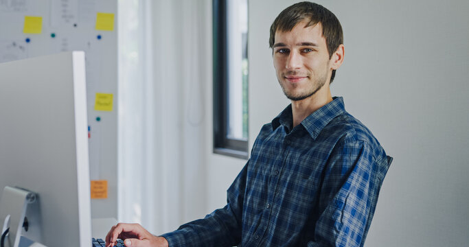 Portrait confident smiling male programmer working with robotics code AI software and looking at camera in tech office. Artificial intelligence dashboard, robotics, user interface, machine learning.