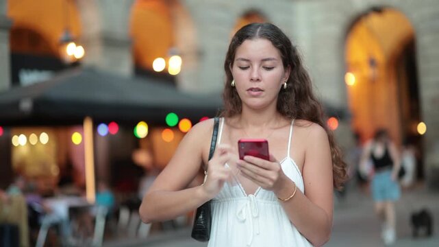 Young woman in summer clothes and with a phone in hands walks through the streets of Barcelona, she wants to meet friends and go to a restaurant in the evening