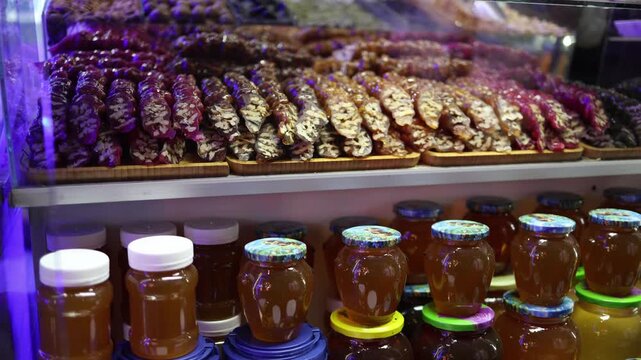 Traditional churchkhela sweets and jars of honey arranged on market shelf rich textures and natural colors showcase local handmade treats in vibrant shop setting