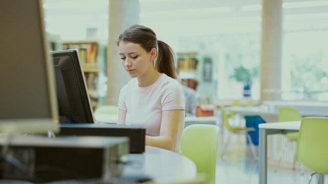 Female student works at computer in library. Studying, using additional online sources of information, searching for information on Internet, prepare to exam