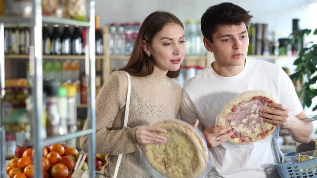 Young satisfied family couple choosing chilled pizza in small market