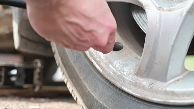 A person uses a tire pressure gauge to check the pressure of a vehicle tire before attaching an air compressor hose to inflate it