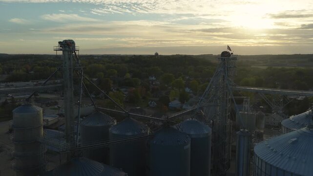 Row of grain silos and elevators at sunset overlooking farmland in Pine Island Minnesota, aerial fly through