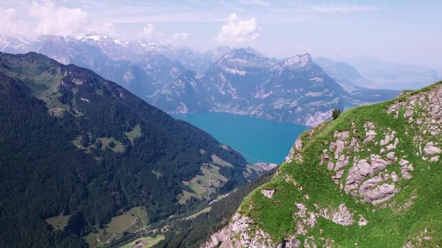 Drone view of Stoos Ridge revealing steep green cliffs, deep alpine valleys, and a turquoise Swiss lake framed by rugged mountain peaks.