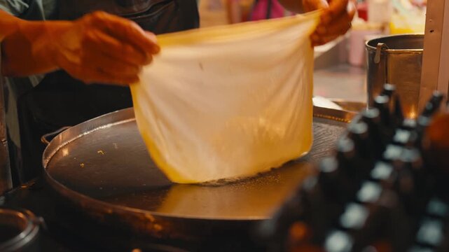 Street food vendor cooking roti dough on a hot metal pan at night time