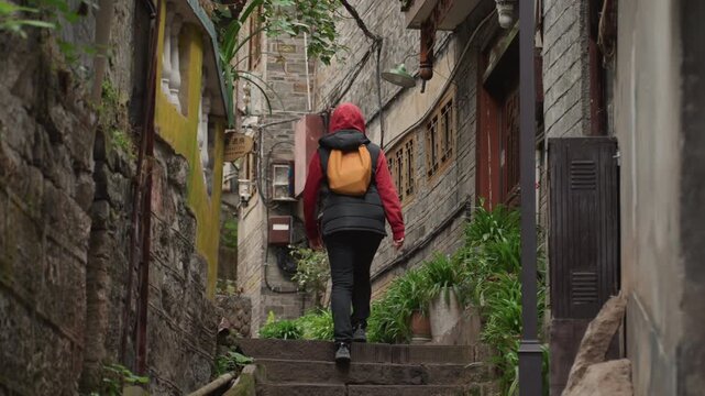 White commuter walking historic stone steps through mossy narrow laneway, carrying yellow backpack, steady pace and casual stride, vintage doors and iron rail details, damp weather and textured walls,