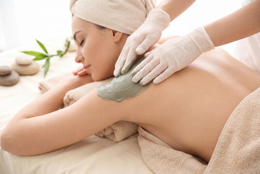 Woman receiving a clay body mask treatment on her shoulder at a spa