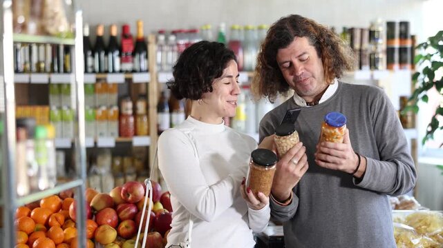 Spouses gets acquainted with food scan QR code, take reading canned beans and lentils label using phone camera in shop. Client view legume package, inspect manufacturer information using mobile app