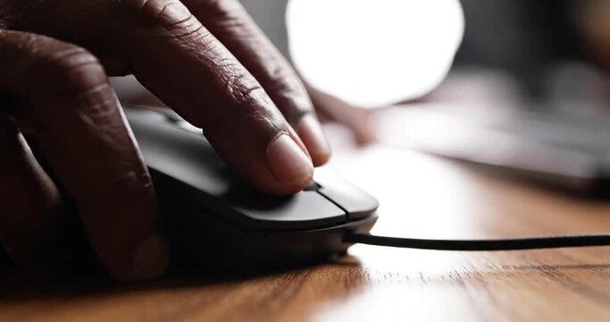 Close-up of a hand using a computer mouse on a wooden desk with blurred background elements