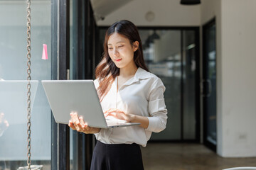 Fototapeta premium Young businesswoman standing typing on laptop workspace