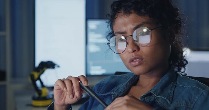 Close-up young Black female programmer coding AI software on multiple screens in night office. Network security, cybersecurity, machine learning, working late, overtime, robotics automation concept.