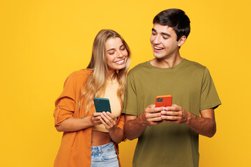 Naklejka premium Young smiling happy satisfied couple friends family man woman wear casual clothes hold in hand use mobile cell phone together isolated on pastel plain light yellow color background studio portrait