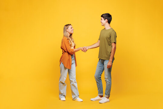 Full body side view young smiling fun couple two friends family man woman wear casual clothes look to each other shaking hands together isolated on pastel plain light yellow color background studio