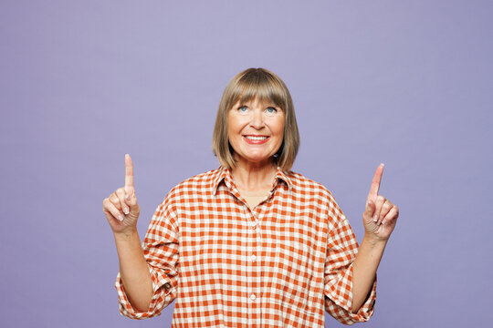 Elderly blonde happy woman 50s year old wear beige t-shirt shirt casual clothes point index finger overhead indicate on area mock up isolated on plain pastel light purple background Lifestyle concept