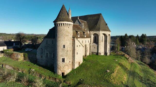 Side view of historic Saint Angel romanesque stone church with prominent conical tower on green hill in Correze France under clear blue sky