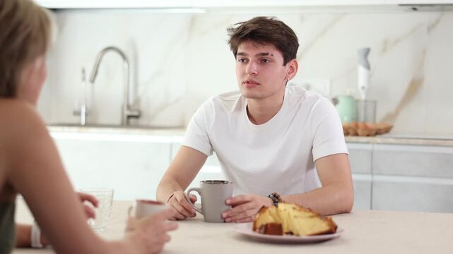 Woman visited guy friend and is chatting sweetly and drinking coffee tea. Positive friend tells about successful vacation, success at work 