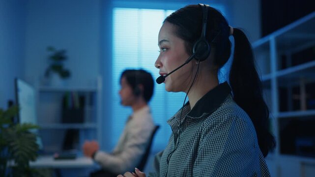 Gen z Asia young call center team or customer support service executive use computer and microphone headset work technical e commerce support in late night office. Telemarketing or sales job concept.