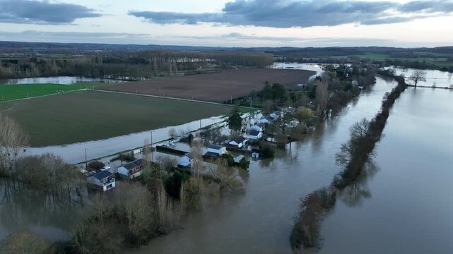 Aerial view of flooded houses and fields in Sarthe department with brown water covering roads and vegetation under dramatic cloudy sky