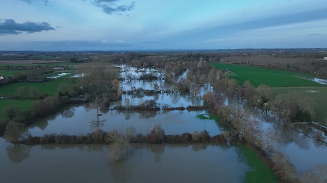 Aerial view of flooded landscape in Sarthe department with large areas of calm brown water reflecting the sky and surrounding green fields