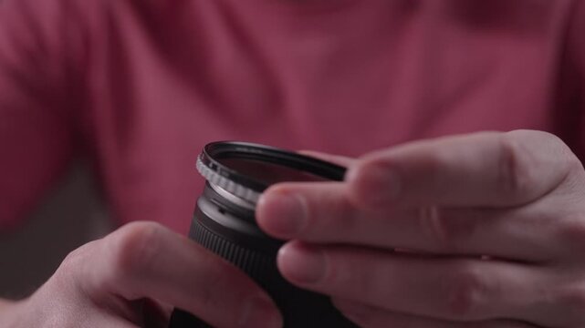 Photographer unscrewing polarizing filter from dslr or mirrorless camera lens during equipment maintenance and cleaning for professional video or photo shoot, close-up. Shooting in slow motion.
