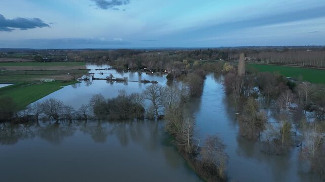 Aerial view of extensive flooding in Sarthe department with wide brown water covering fields and trees under blue evening sky