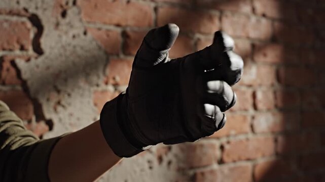 A close-up shot of a gloved hand making a fist in front of a dimly lit brick wall during a police raid operation.